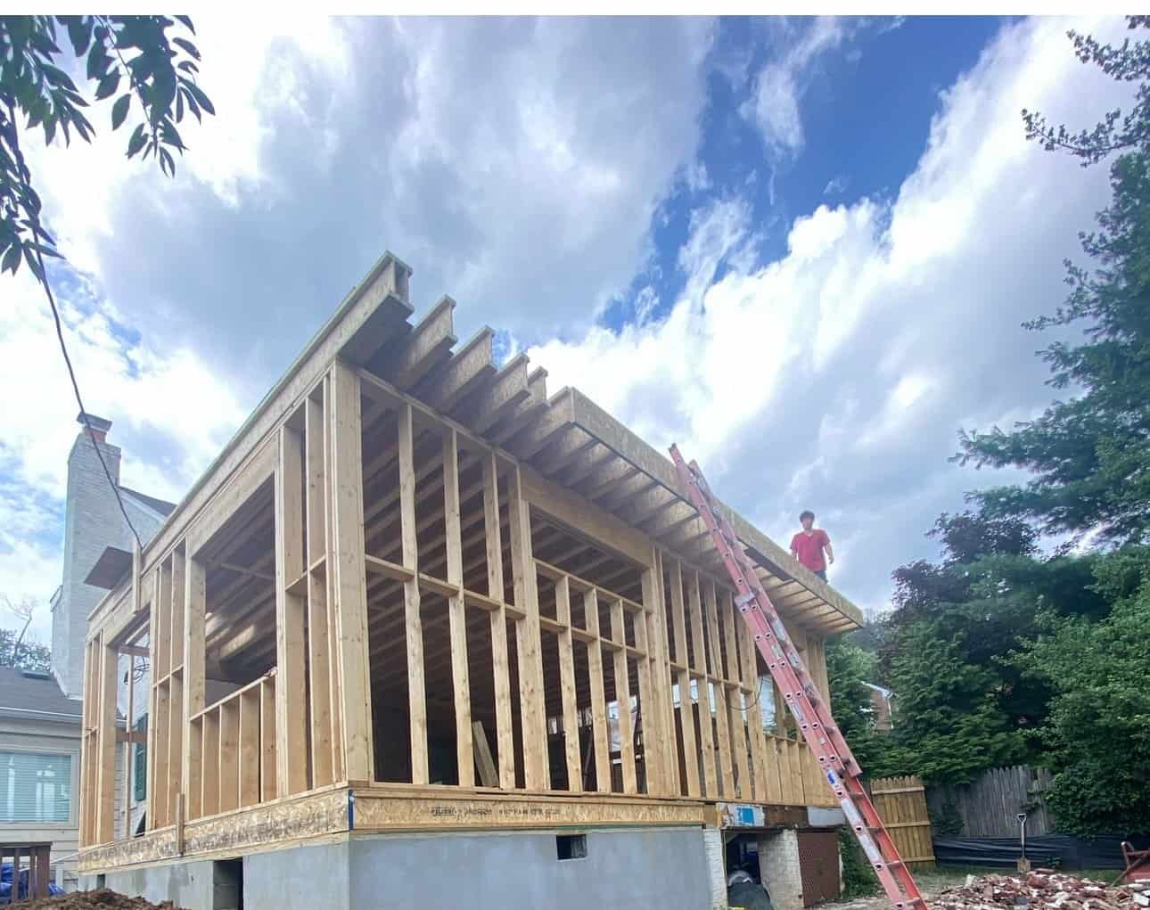 Custom home framing in progress with wooden structure and blue sky background.