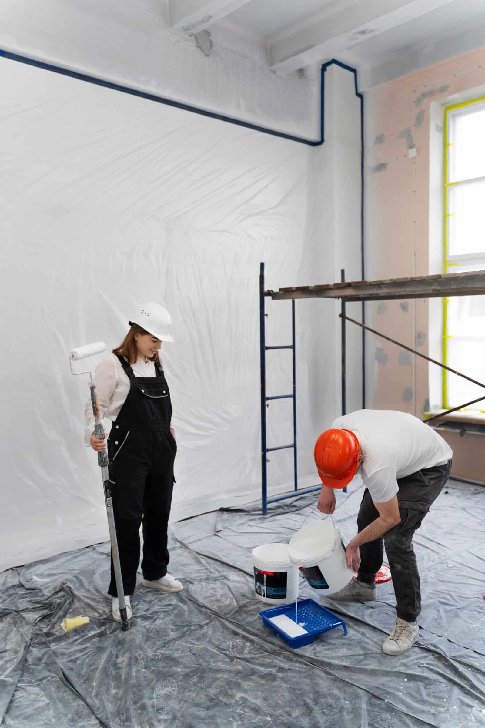 Handyman painting a wall with a roller brush in a room under renovation.