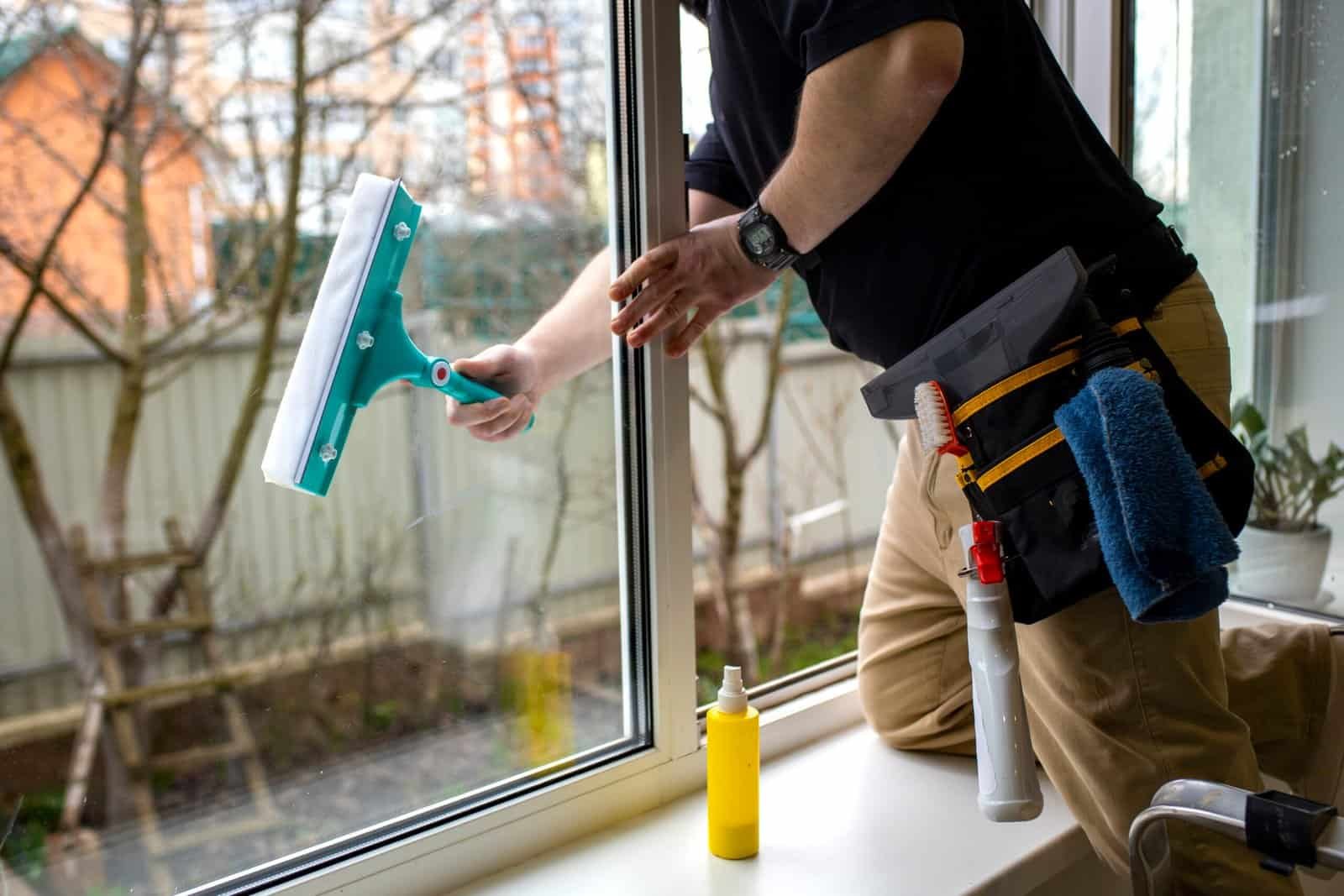 Professional window cleaning by handyman with squeegee and tools.