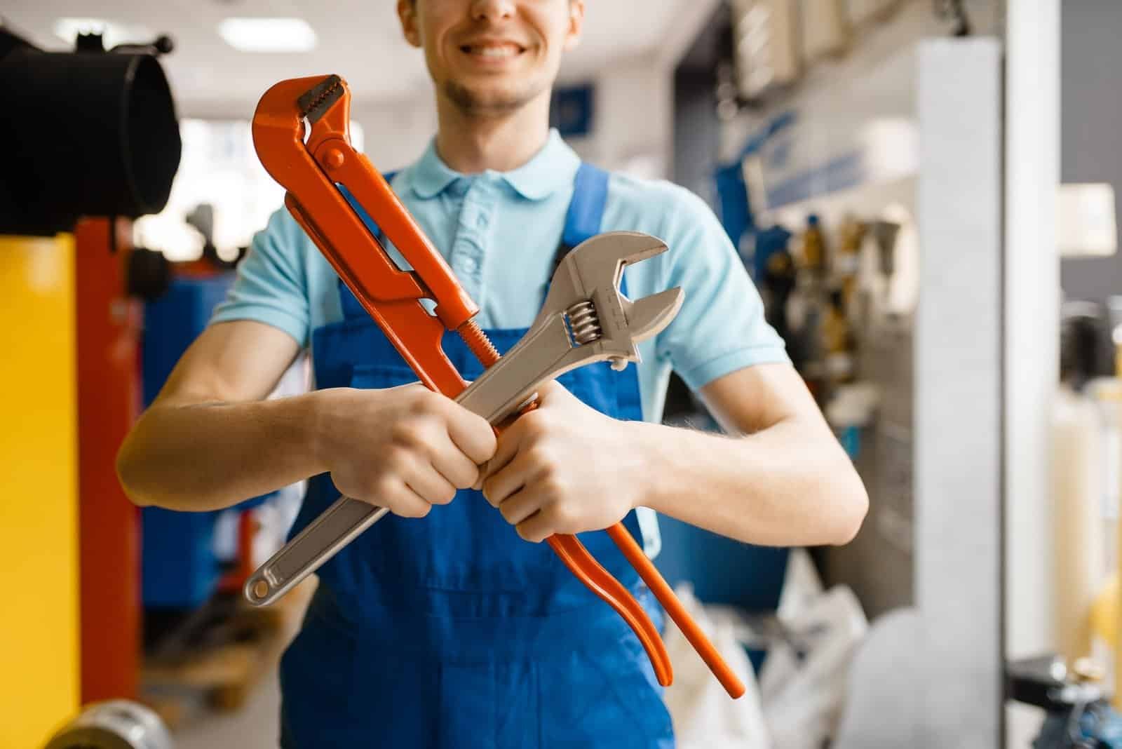 Skilled handyman holding adjustable wrench and pipe wrench in workshop.